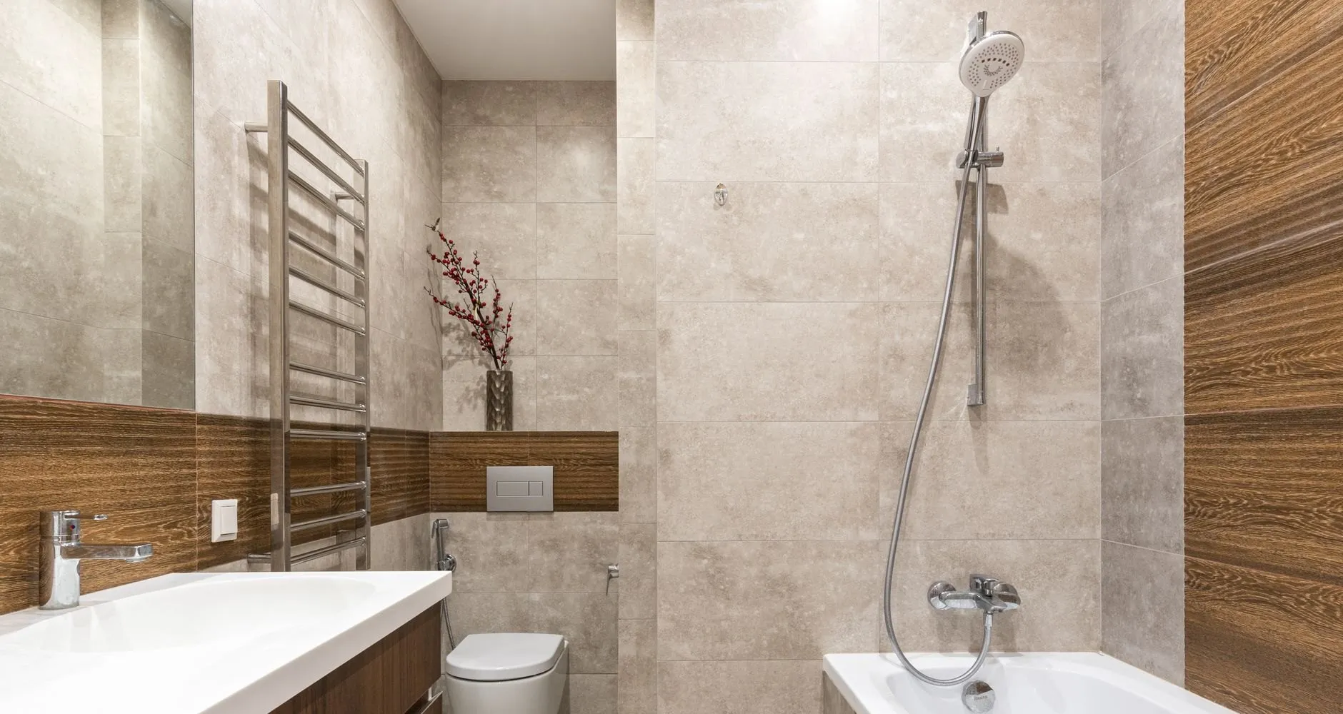 The finished bathroom: stone-effect tiles with a walnut-look band, a built-in bath with a shower rail, a wall-hung WC and a chrome towel ladder