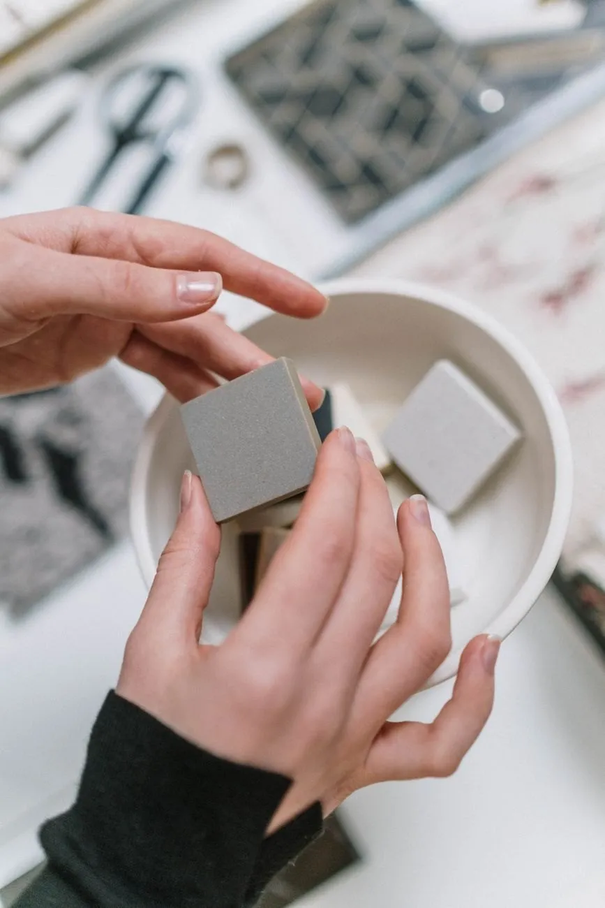 Hands holding small grey and white ceramic tile samples over a bowl on a design table