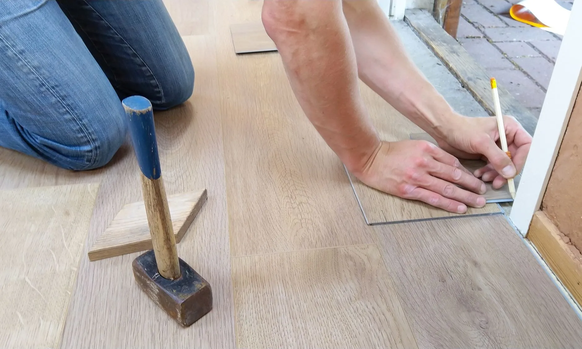 A fitter kneeling on a new oak-effect floor, marking a plank with a pencil and square beside a mallet